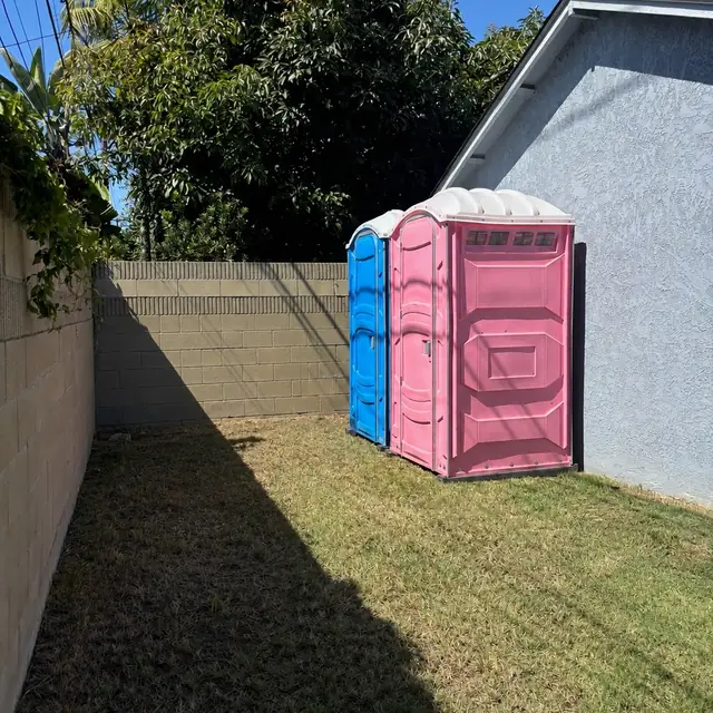 Two porta potties in a fenced backyard for a party