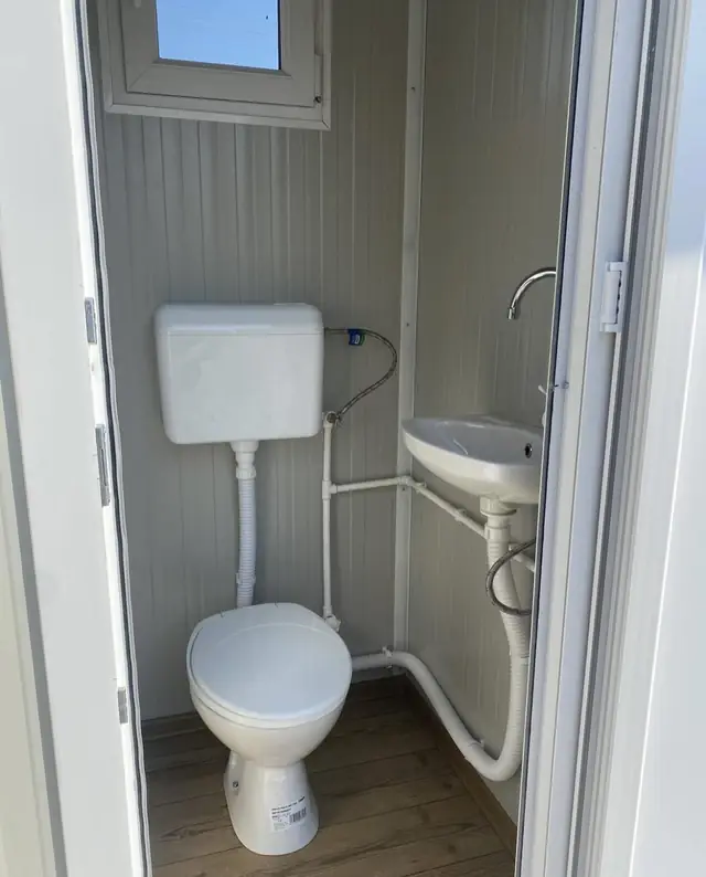 Flushing toilet and corner sink inside a white restroom cabin