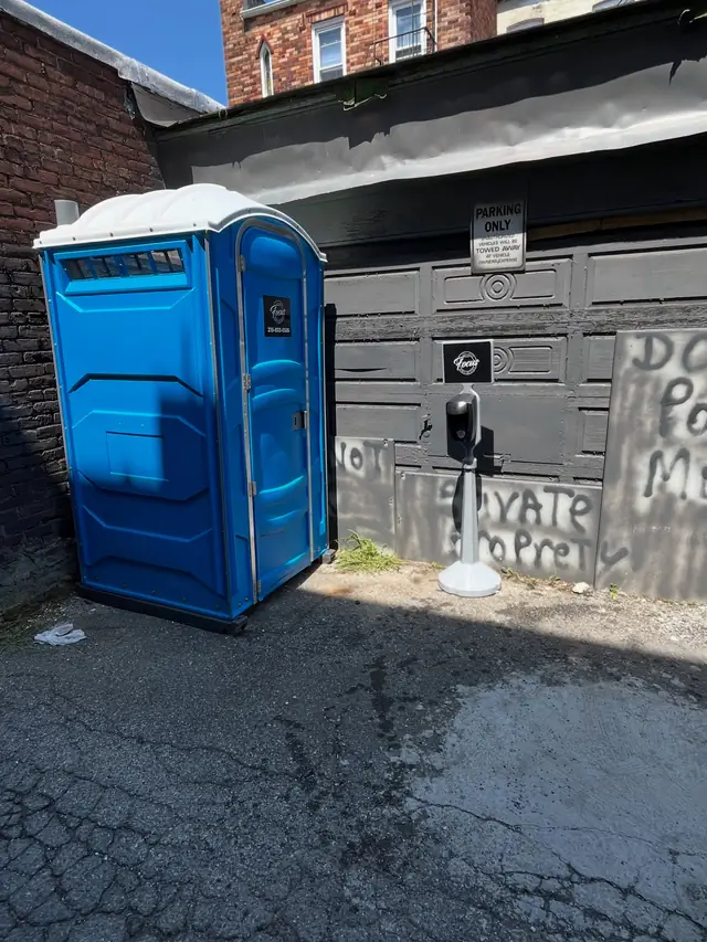 Standard porta potty placed beside a garage on pavement
